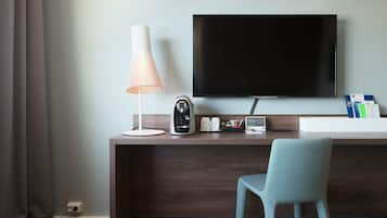 Hotelkamer met een houten bureau, een flatscreen-tv, een lamp, een koffiezetapparaat en een stoel.