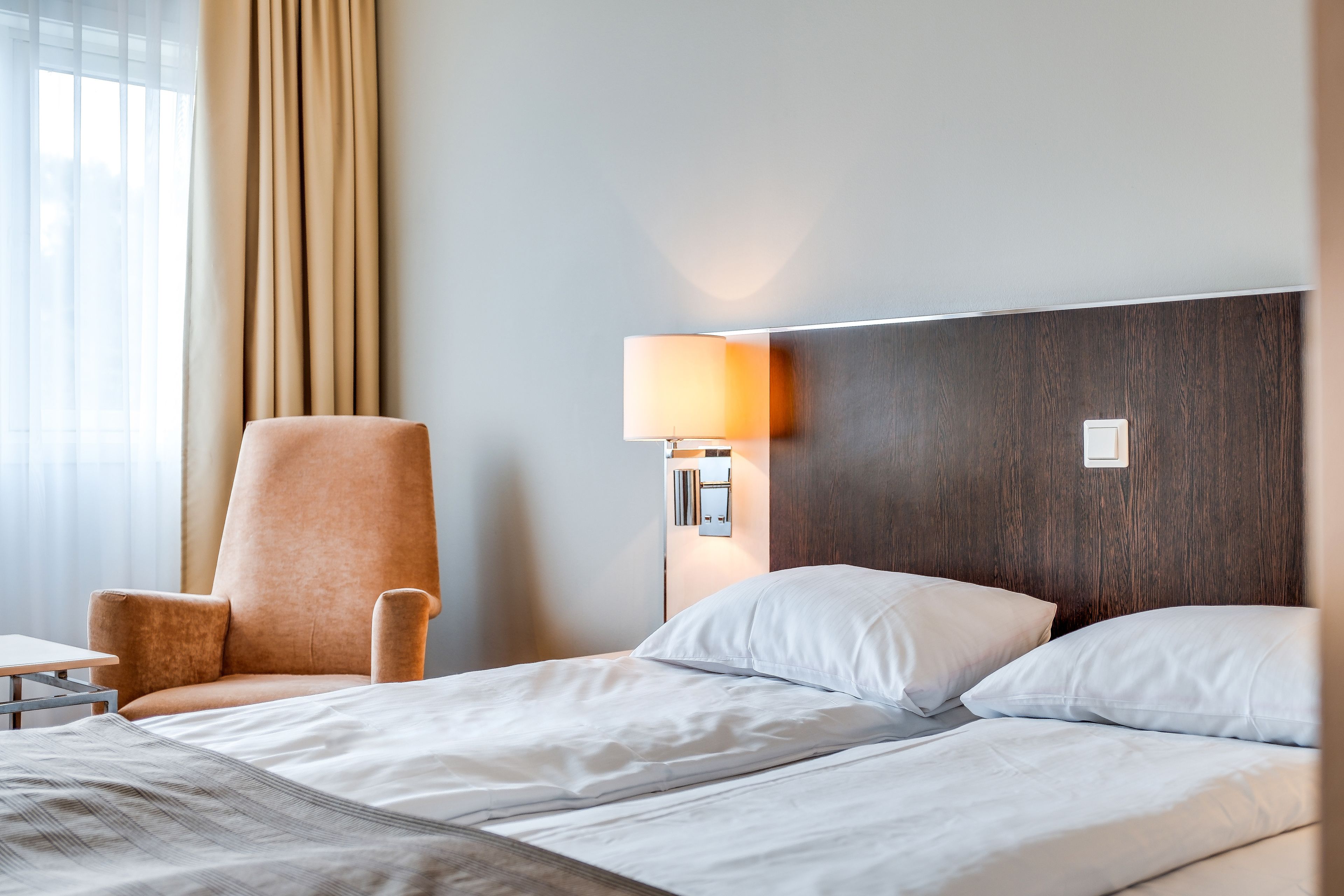A hotel room with a bed, a chair, a lamp, and a window with curtains.