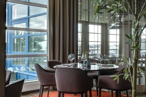 A dining area with a table set for four, large windows, and a potted plant.