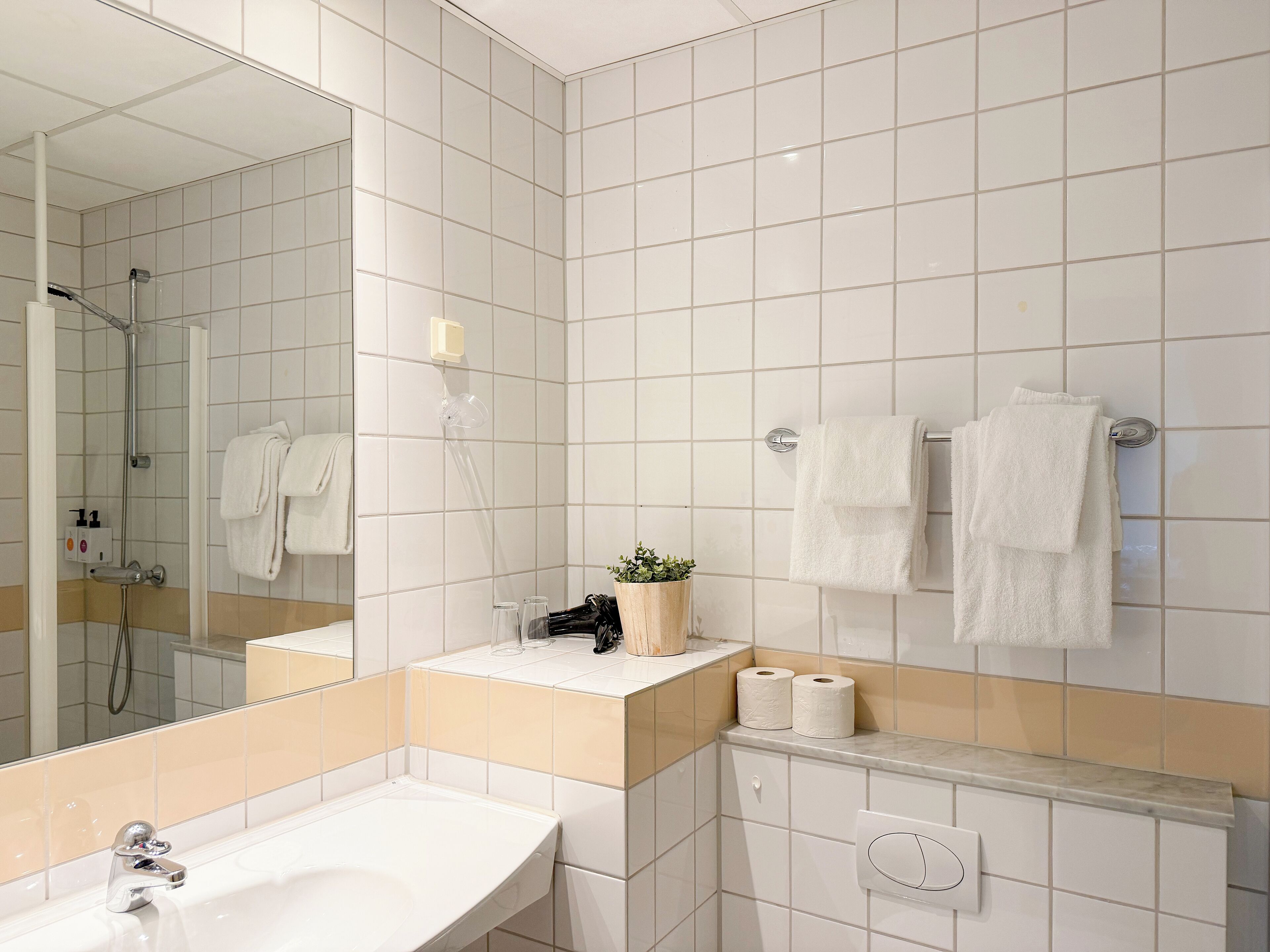 A modern bathroom with a large mirror, a sink, and two towels hanging on the wall.