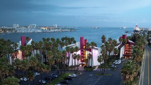 Un hotel con estacionamiento, palmeras y vistas al puerto deportivo y al horizonte de la ciudad.