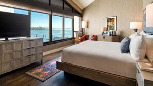 A modern hotel room with a large bed, a TV, a desk, and a view of the water. - The Maya (Long Beach)