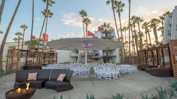 An outdoor patio with round tables and chairs, a fire pit, and a large umbrella.