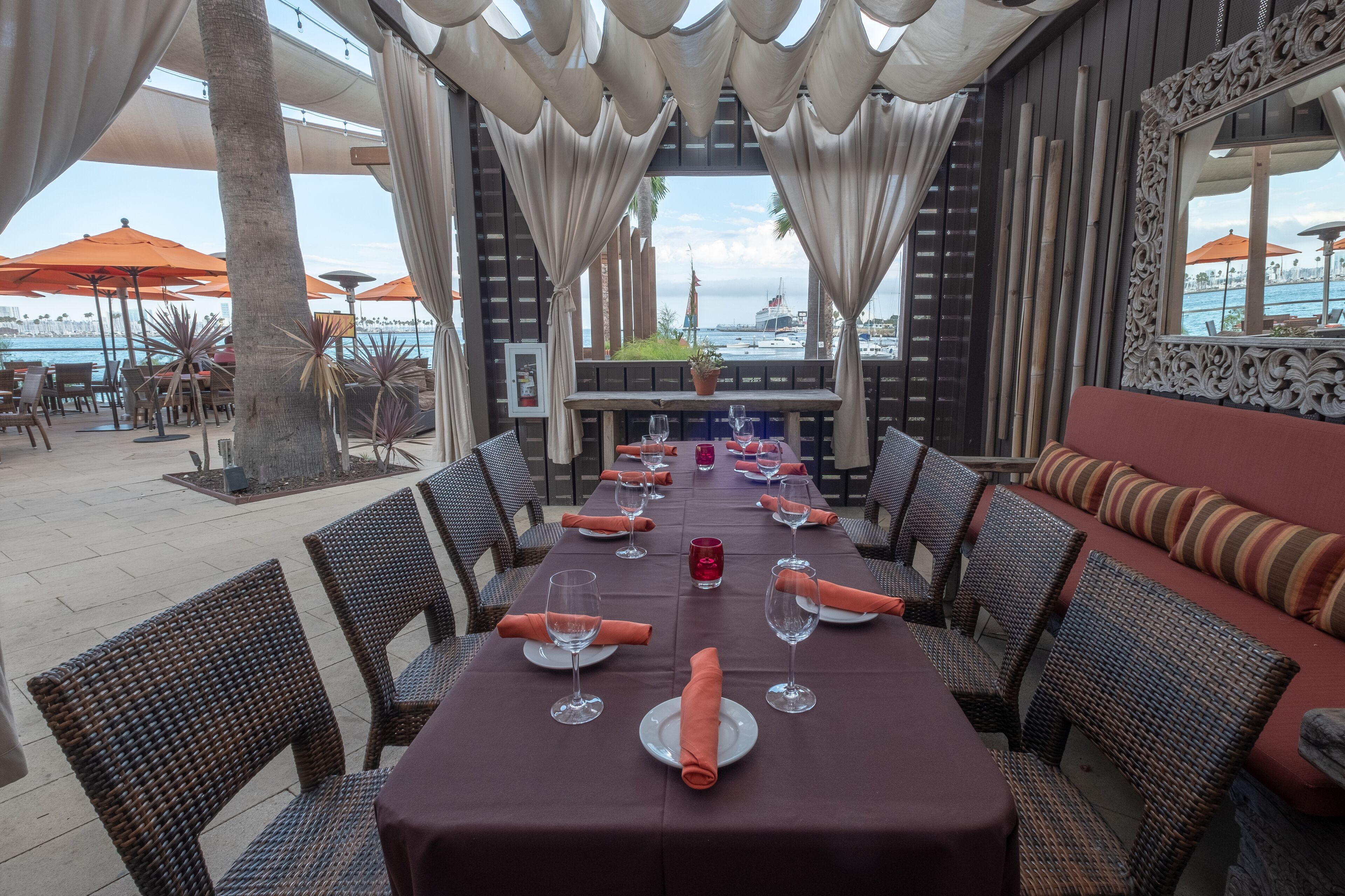 A restaurant with a long table set for dining, outdoor seating, and a view of the water.