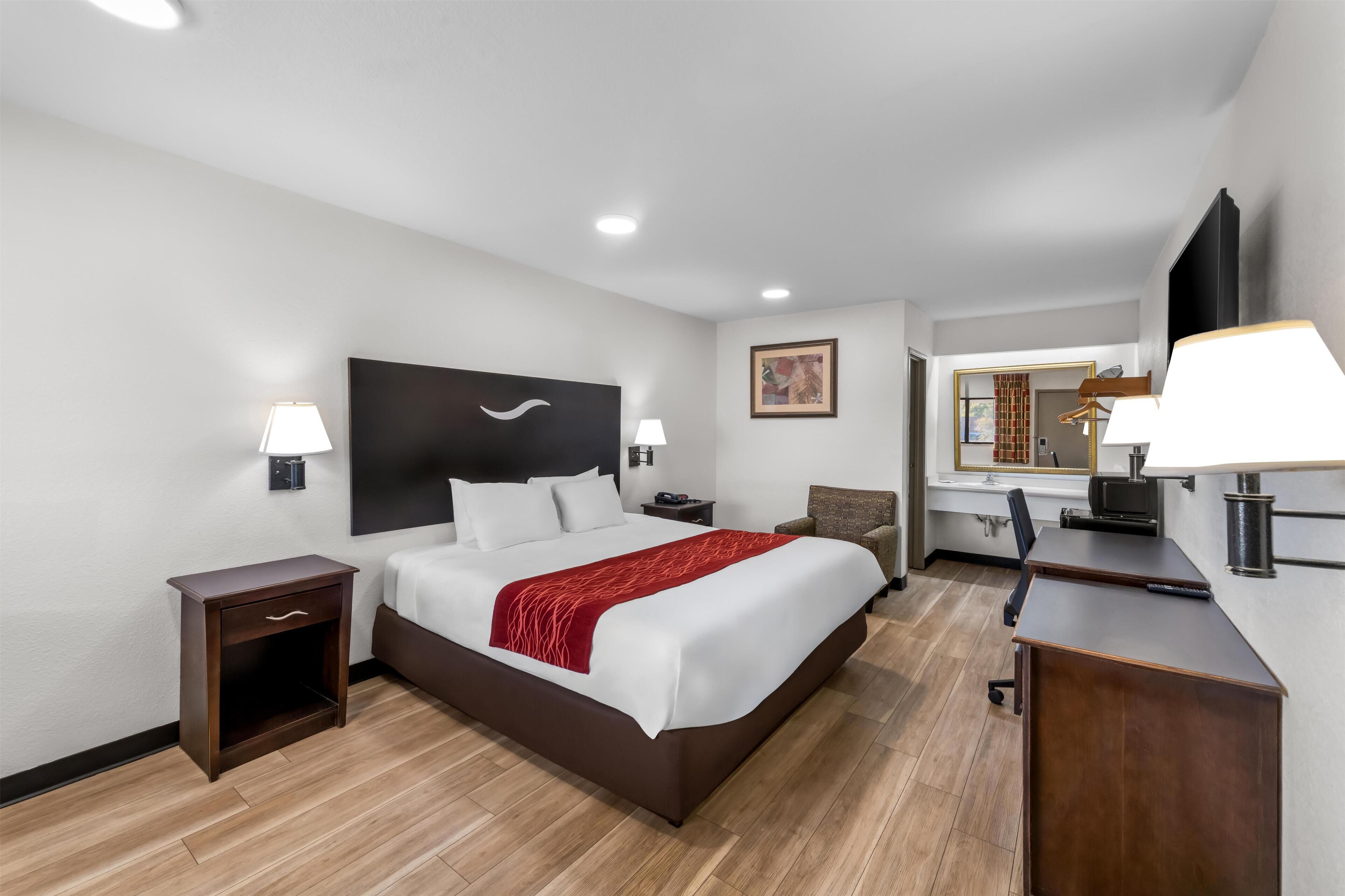 A hotel room with a bed, bedside tables, a desk, a chair, a mirror, and a painting on the wall.