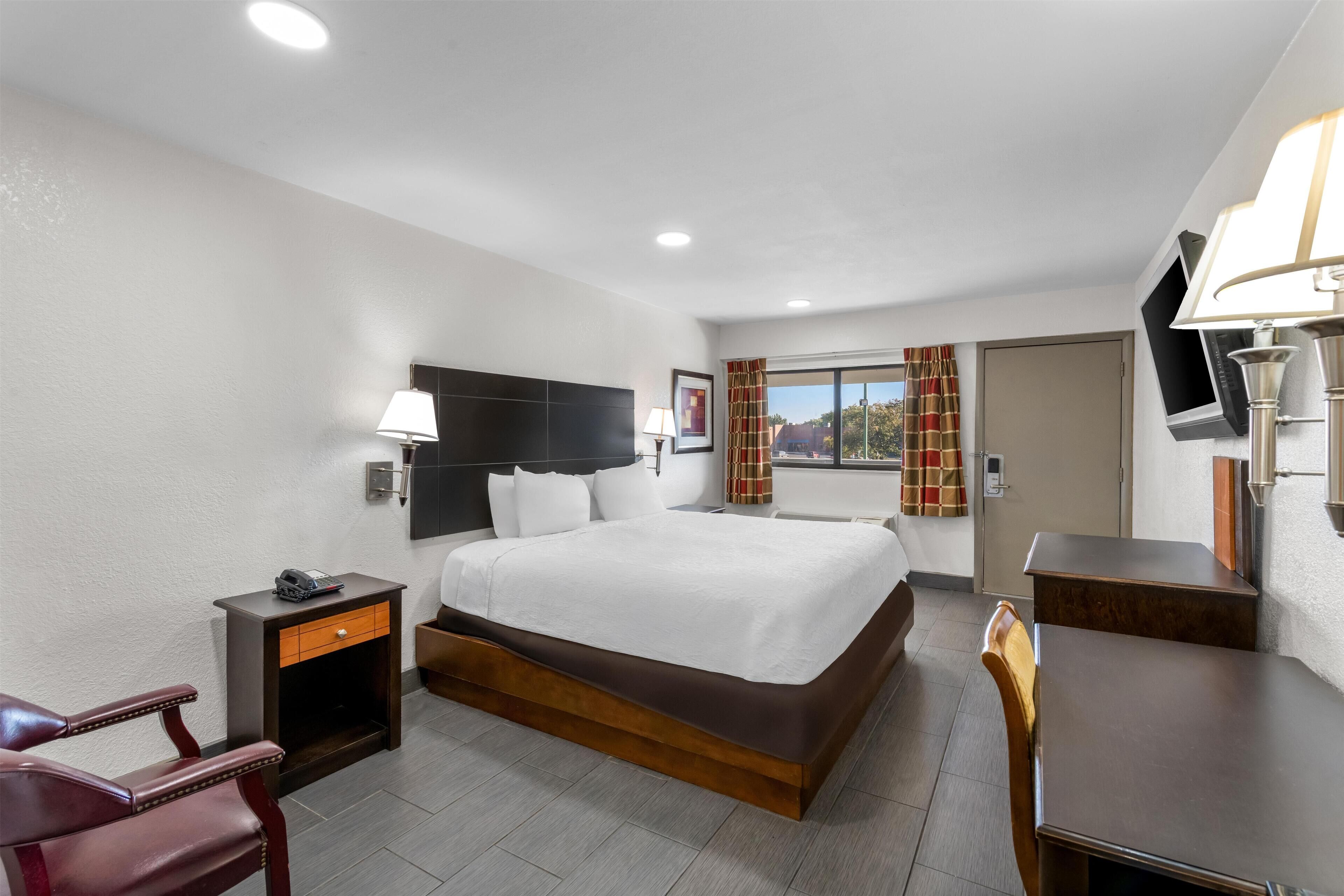 A hotel room with a bed, bedside table, chair, desk, and a TV mounted on the wall.
