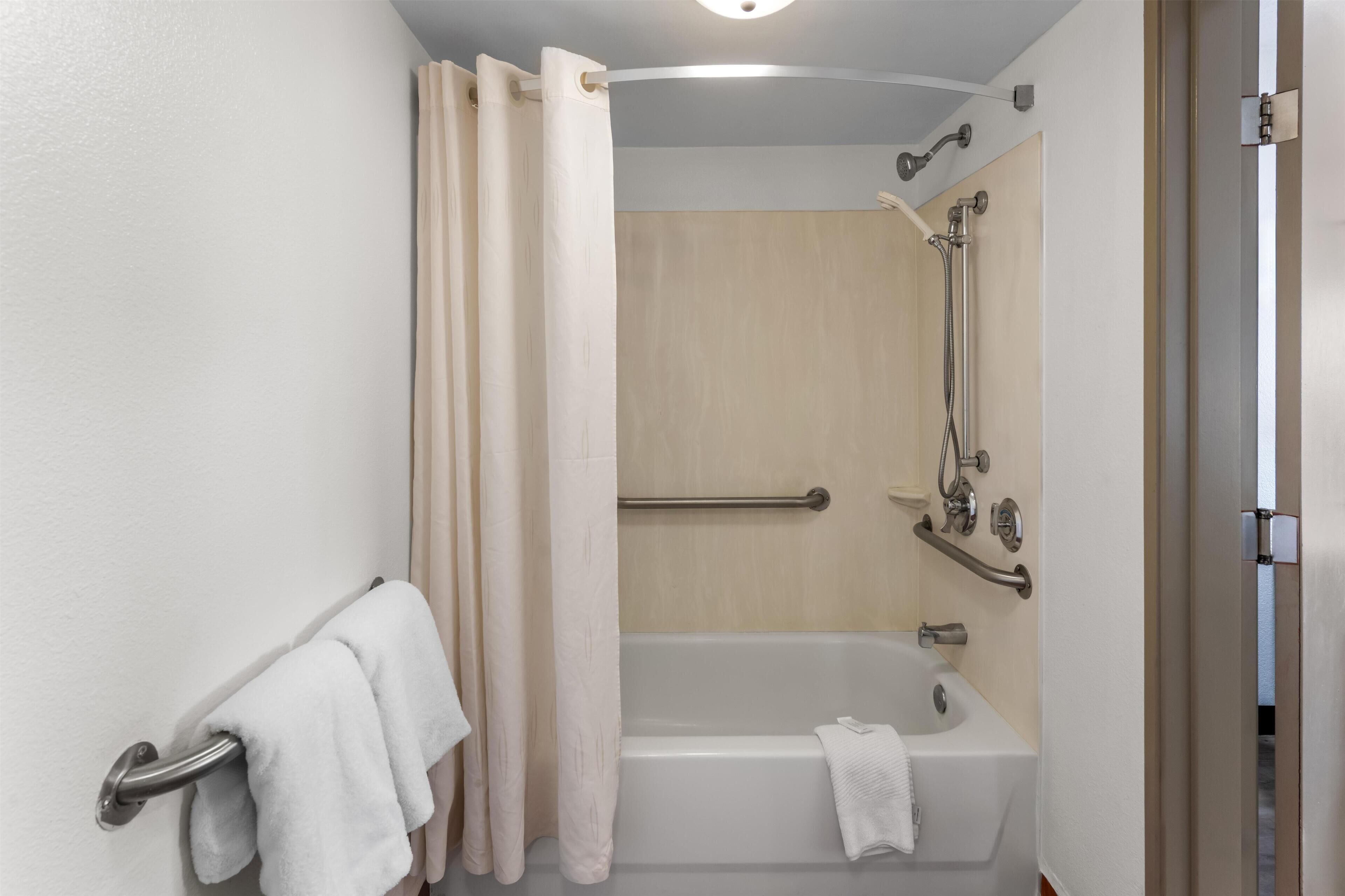 A bathroom with a bathtub, a shower, and a handrail.