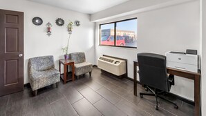 A room with a brown door, two patterned chairs, a small table with a plant, a window with a red car view, and a desk with a printer. - Americas Best Value Inn Kansas City E Independence (Independence)