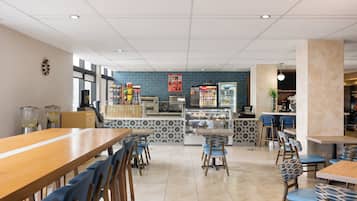 L’intérieur d’un restaurant présente une longue table en bois, des chaises à motifs bleus, un comptoir où sont exposés des plats, et un mur recouvert de carreaux.