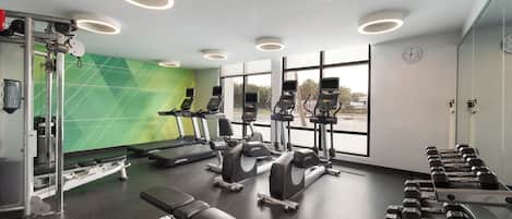 A gym with cardio machines, dumbbells, and weight benches.