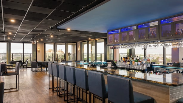 A bar area with a long counter, bar stools, and a city view through large windows. - Holiday Inn Miami - International Airport by IHG (Miami Springs)