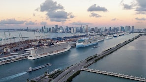 A cruise ship docked at a port with a city skyline in the background.