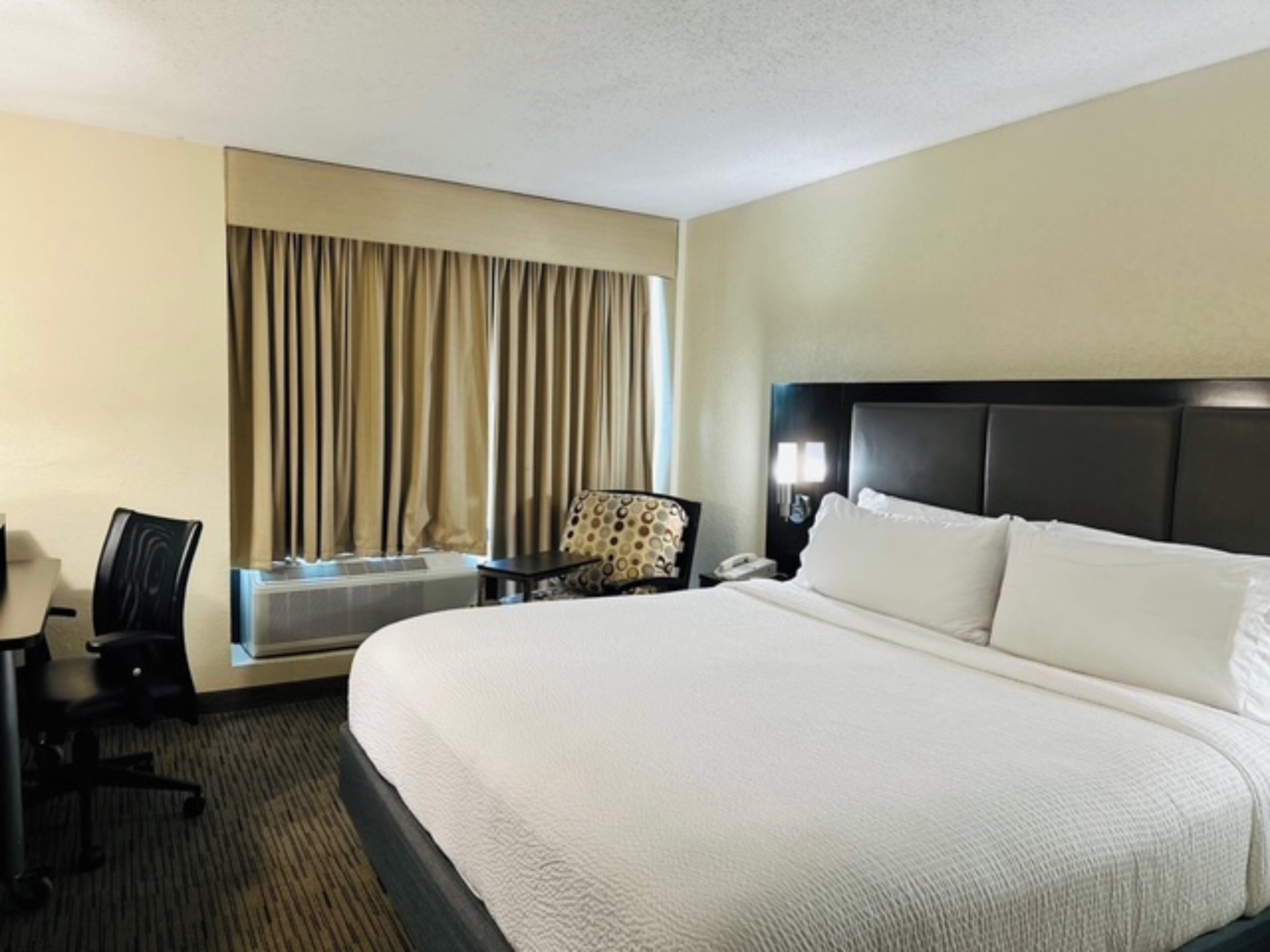 A hotel room with a large bed, a desk, a chair, and a window with curtains.