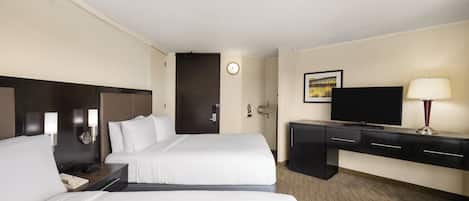 Quarto de hotel com duas camas, uma escrivaninha, televisão e um relógio na parede.