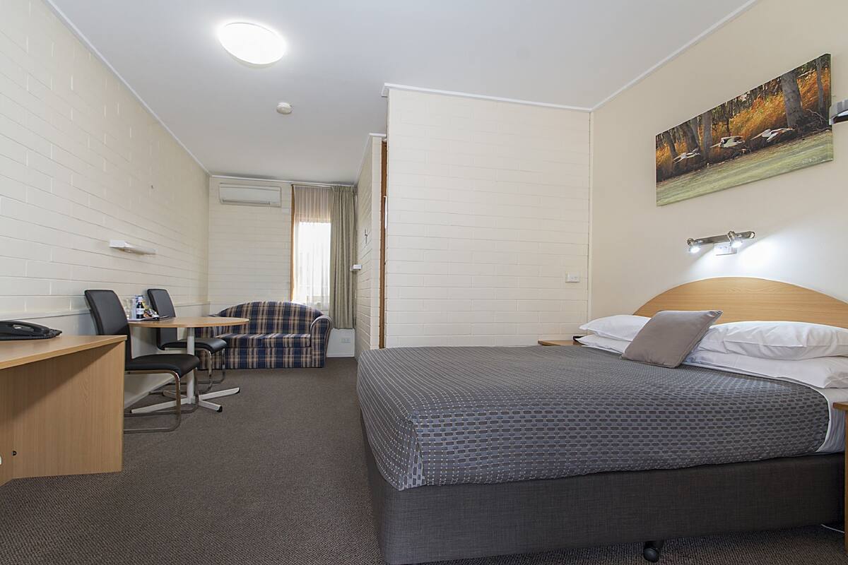 Una habitación de hotel con cama, escritorio, silla, sofá y un cuadro en la pared.