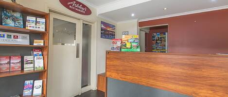 A reception area with a wooden reception desk, a bookshelf with travel brochures, and a sign for Ashley's Restaurant.