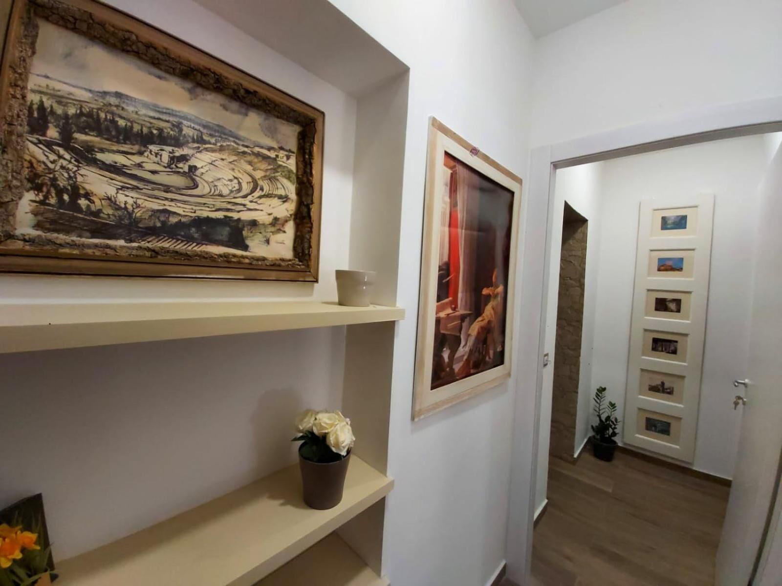 A hallway with artwork on the walls, a potted plant, and a door with a picture gallery.