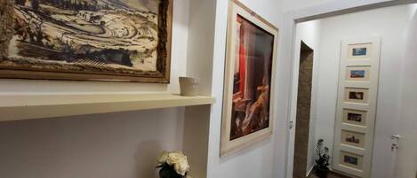 A hallway with artwork on the walls, a potted plant, and a door with a picture gallery.