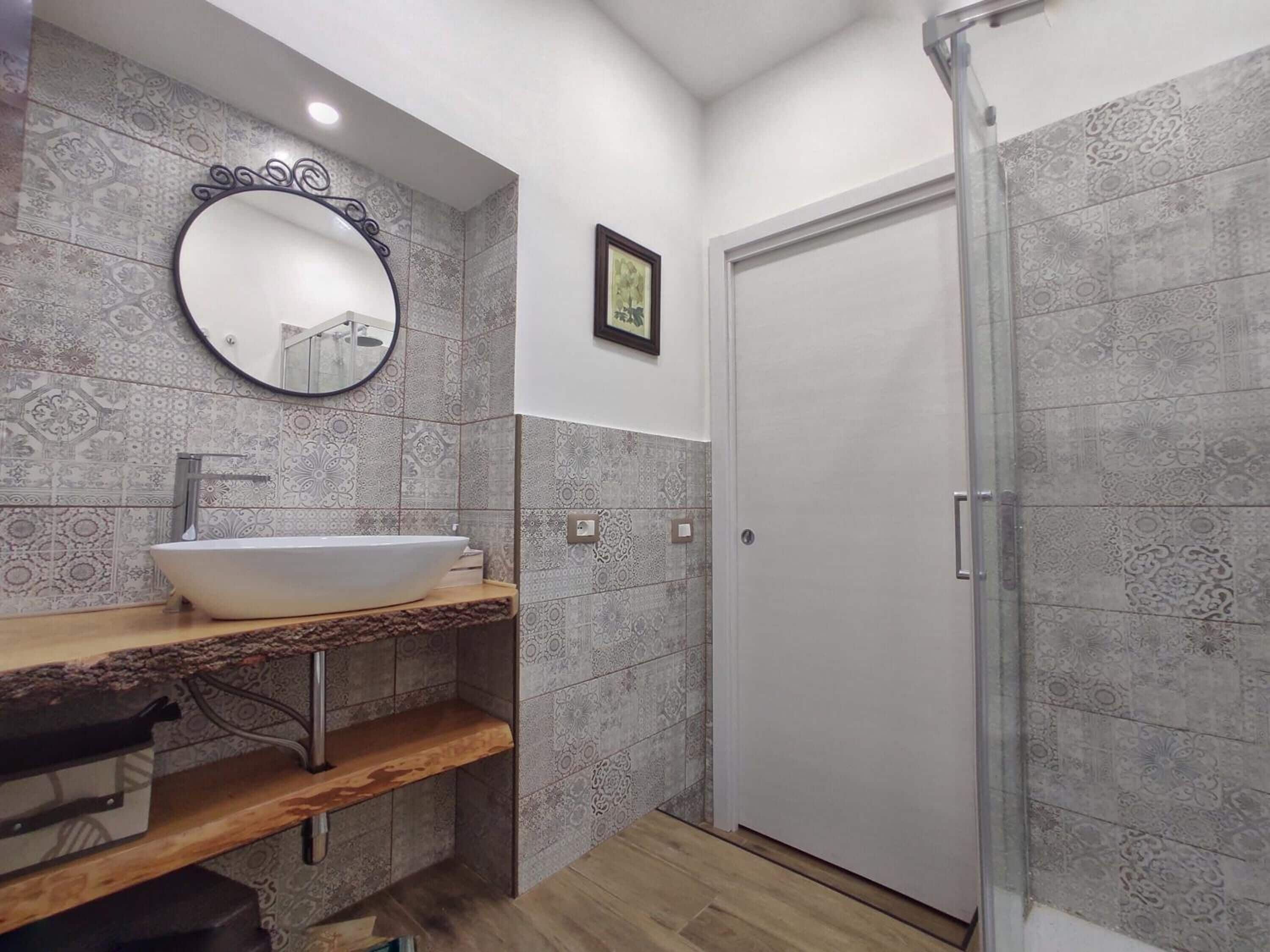 Un baño con lavamanos independiente, un espejo, baldosas estampadas y una puerta.