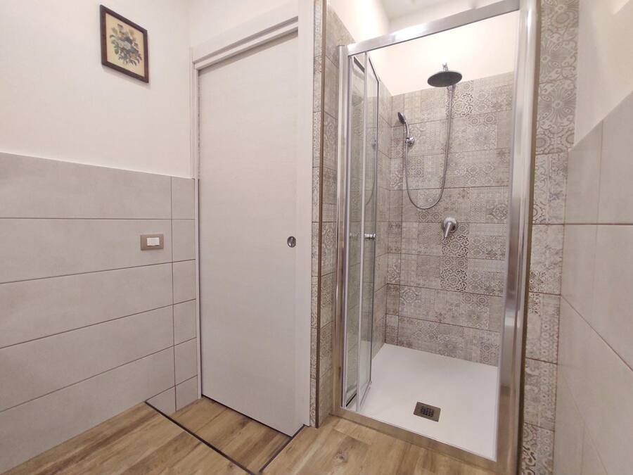 Un baño moderno con ducha envuelta en vidrio, azulejos estampados y suelo de madera.