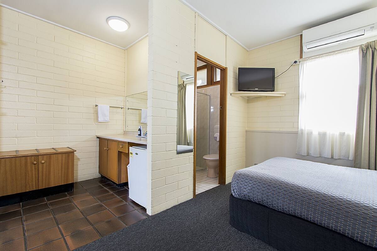 Habitación de hotel con cama, escritorio con espejo, ducha y televisor en la pared.