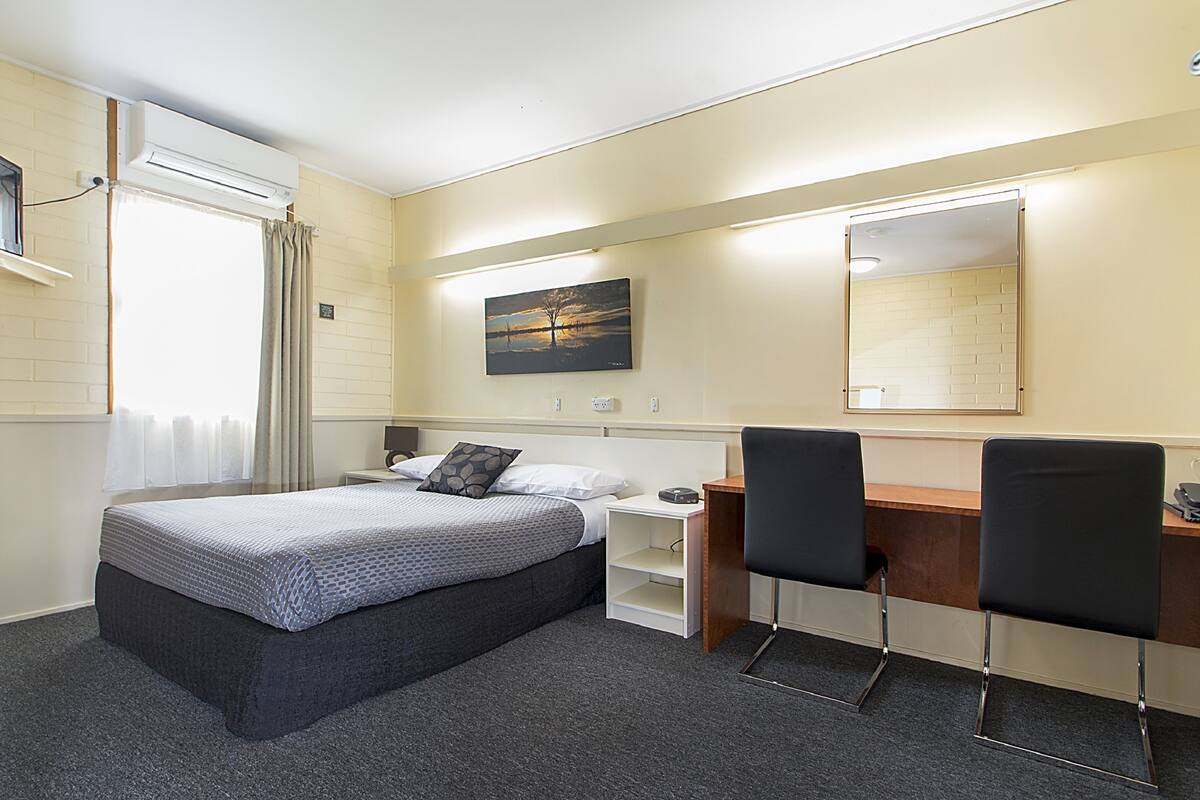 Habitación de hotel con cama, escritorio, sillas y un cuadro en la pared.