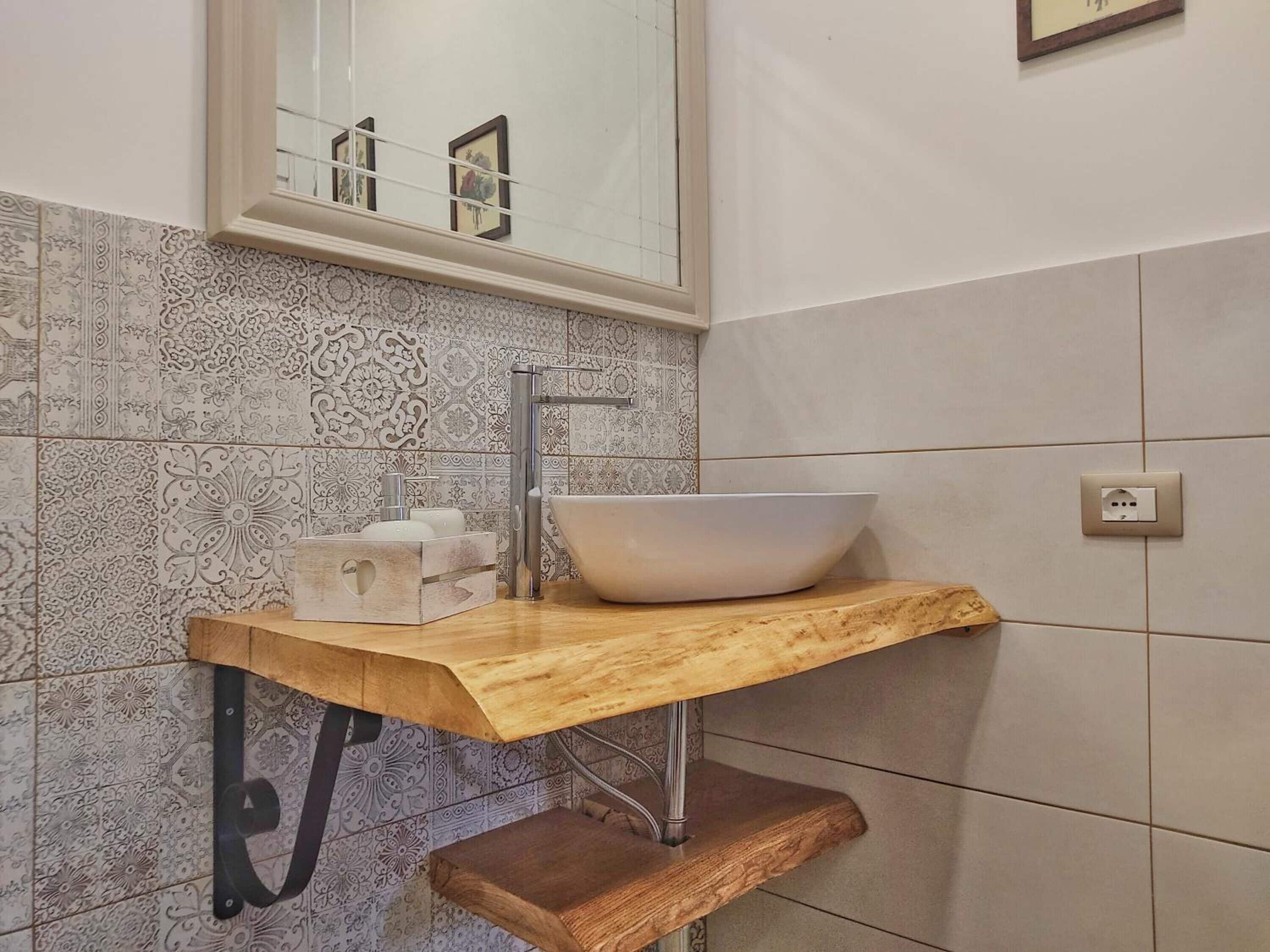A bathroom with a wooden vanity, a white sink, and patterned tiles.