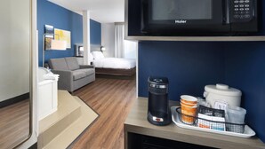 A hotel room with a bed, a gray sofa, a coffee maker, a microwave, and a coffee machine on the counter. - Comfort Suites Outlet Center (Asheville)