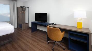 A hotel room with a bed, a desk with a TV, a chair, a lamp, and a wardrobe.