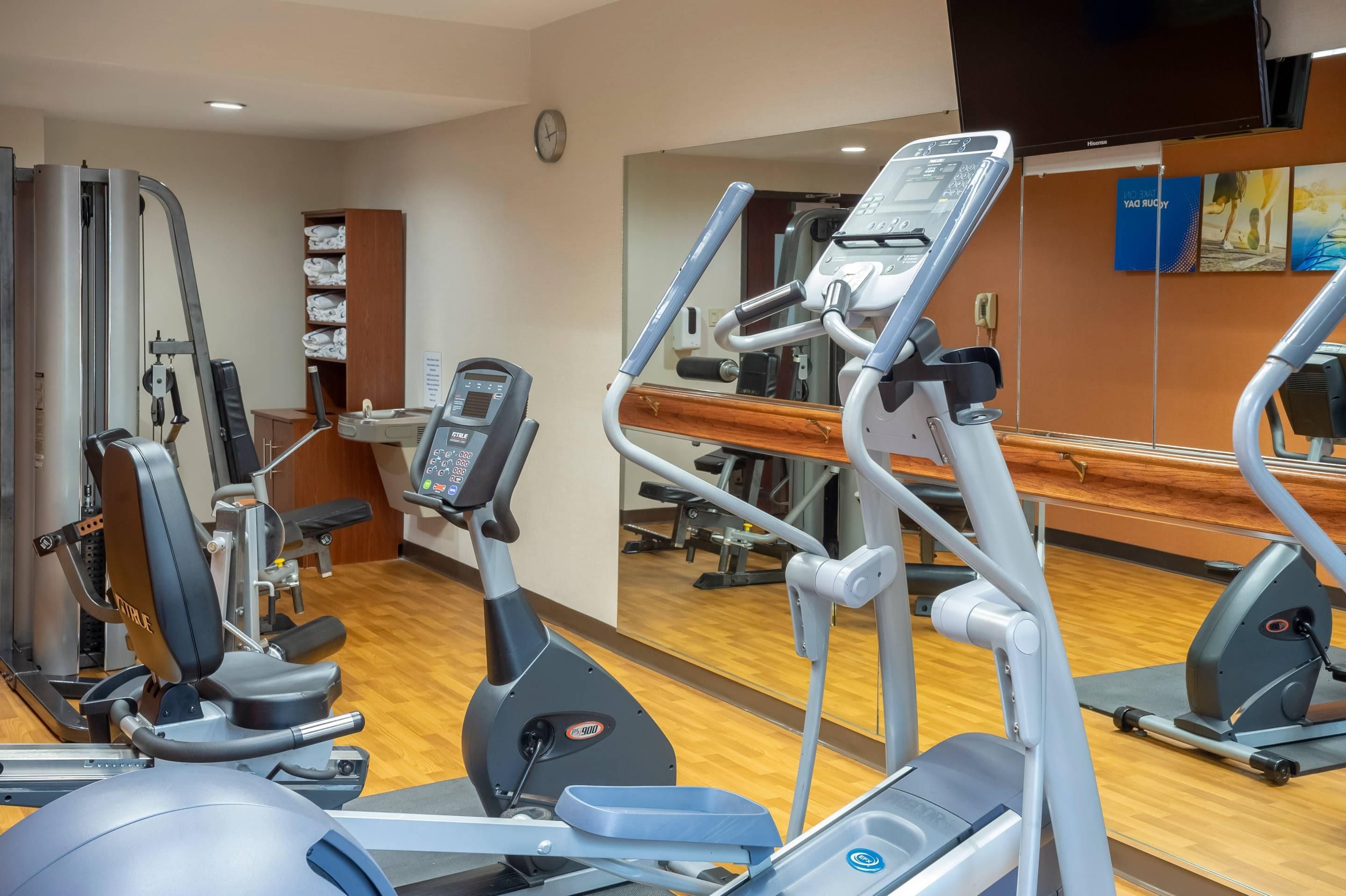 Une salle de sport équipée de divers appareils d’exercice, d’un miroir et d’une horloge au mur.