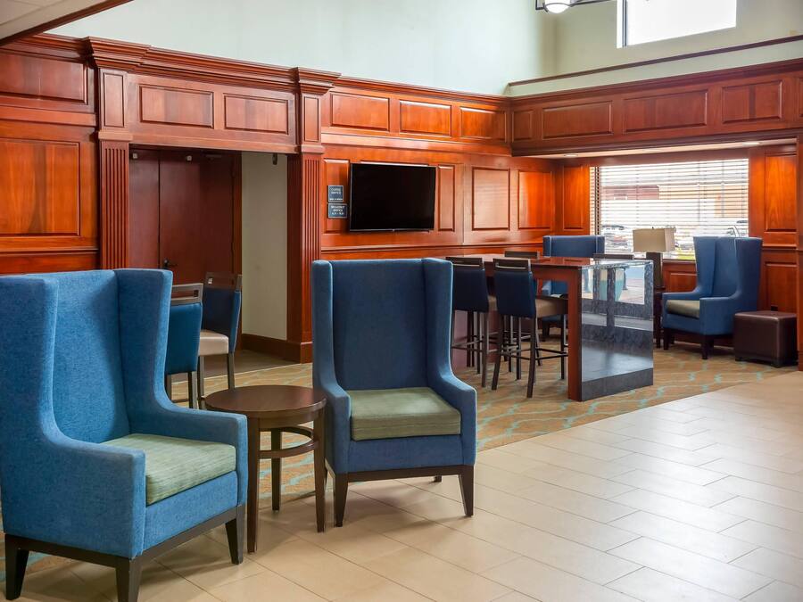 Un hall d’hôtel avec des boiseries, des fauteuils bleus, un panneau indiquant un service de café et un grand écran de télévision.