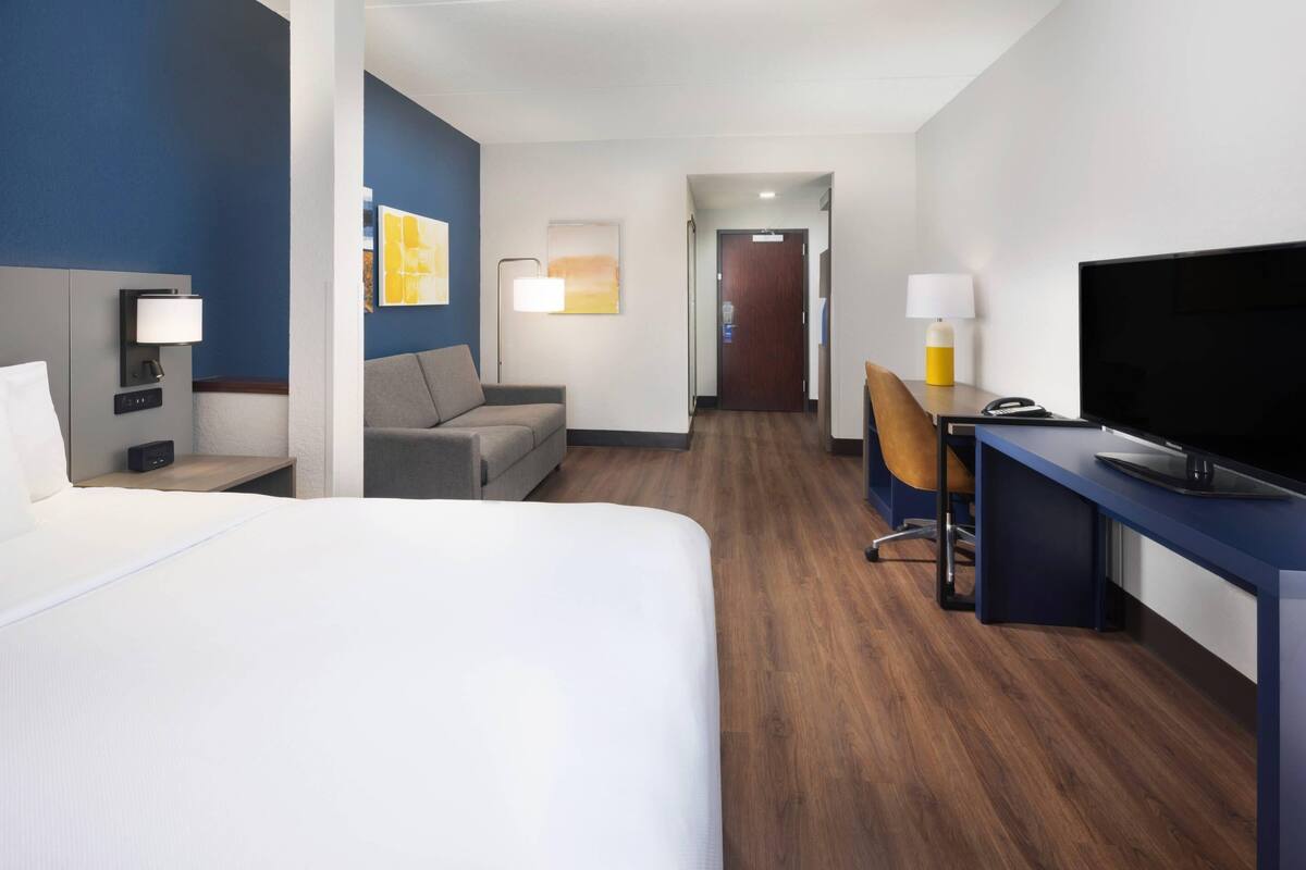 A hotel room with a bed, a desk, a chair, a television, and artwork on the walls.