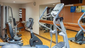 A gym with various exercise machines, a mirror, and a clock on the wall. - Comfort Suites Outlet Center (Asheville)