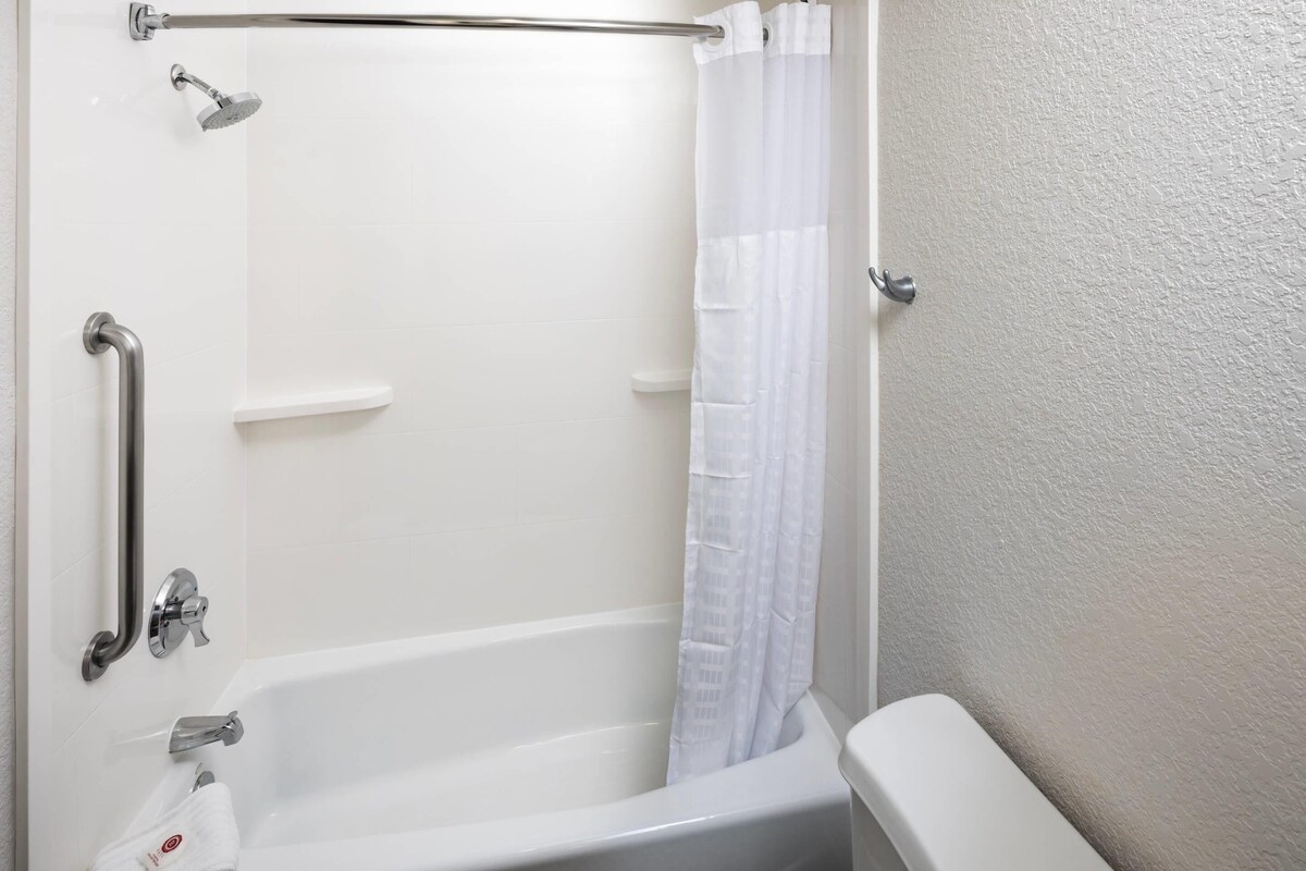 A white bathroom with a bathtub, a showerhead, a grab bar, and a white curtain.