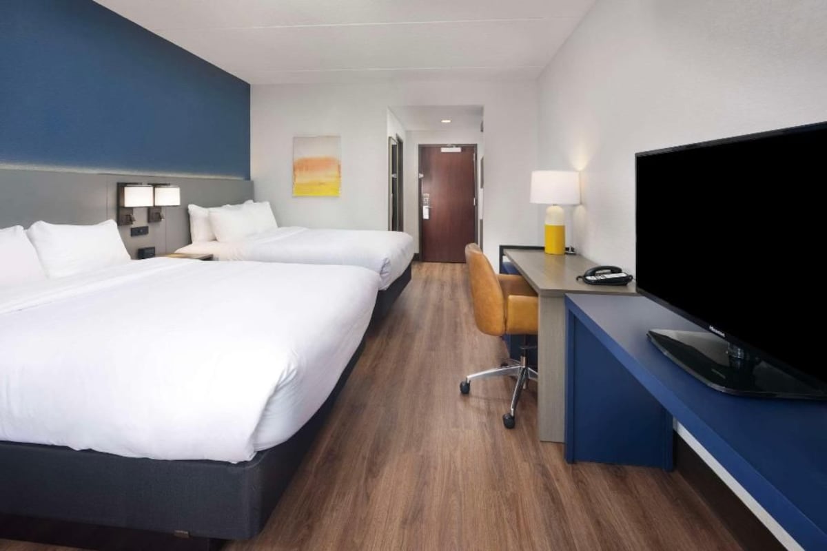 Una camera d'albergo con due letti, una scrivania con televisore e un bagno sullo sfondo.