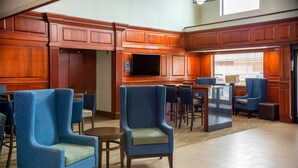 A lobby with wooden paneling, blue armchairs, a flat-screen TV, and a reception desk. - Comfort Suites Outlet Center (Asheville)