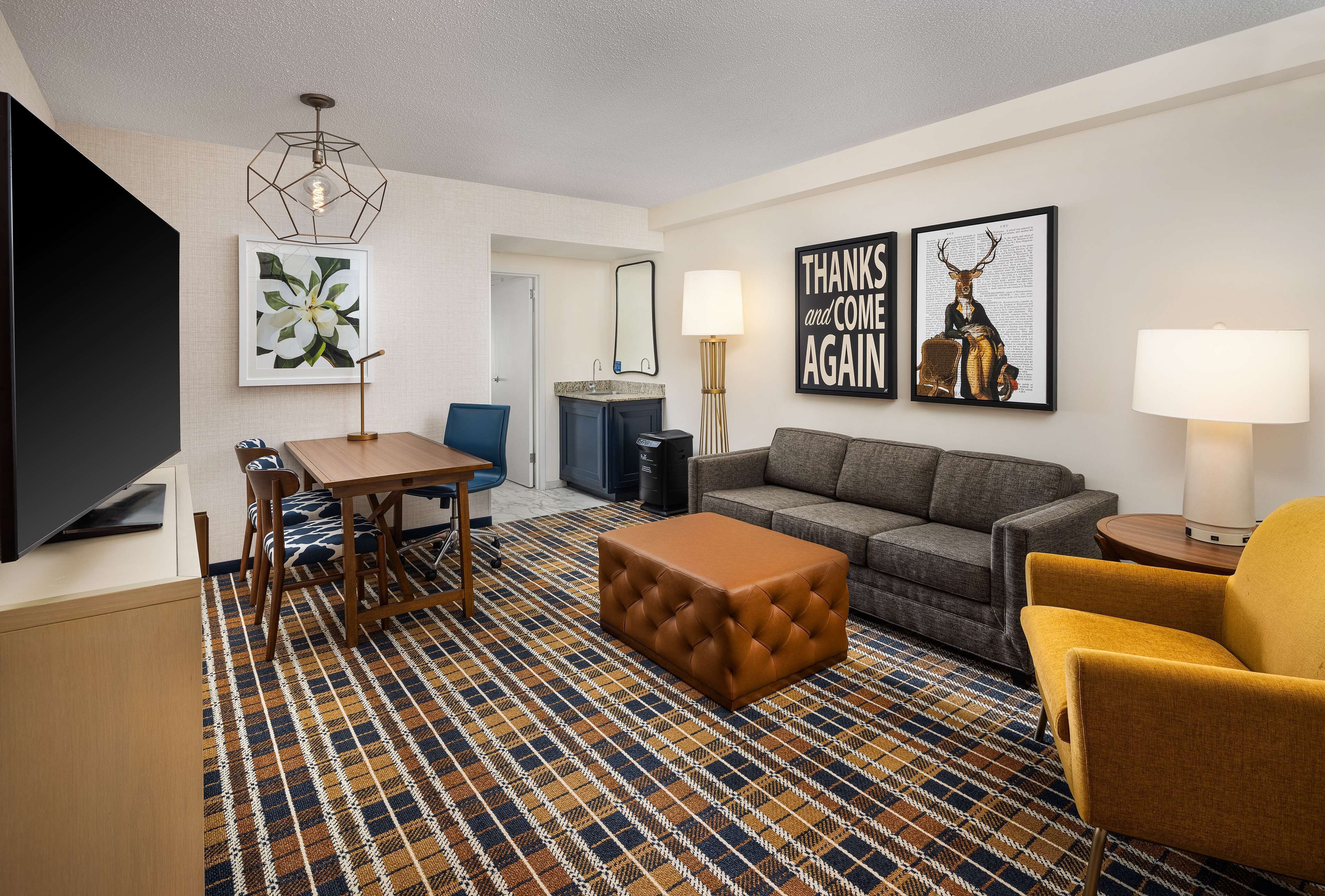 A hotel room with a sofa, armchair, ottoman, dining table, chairs, and artwork on the walls.