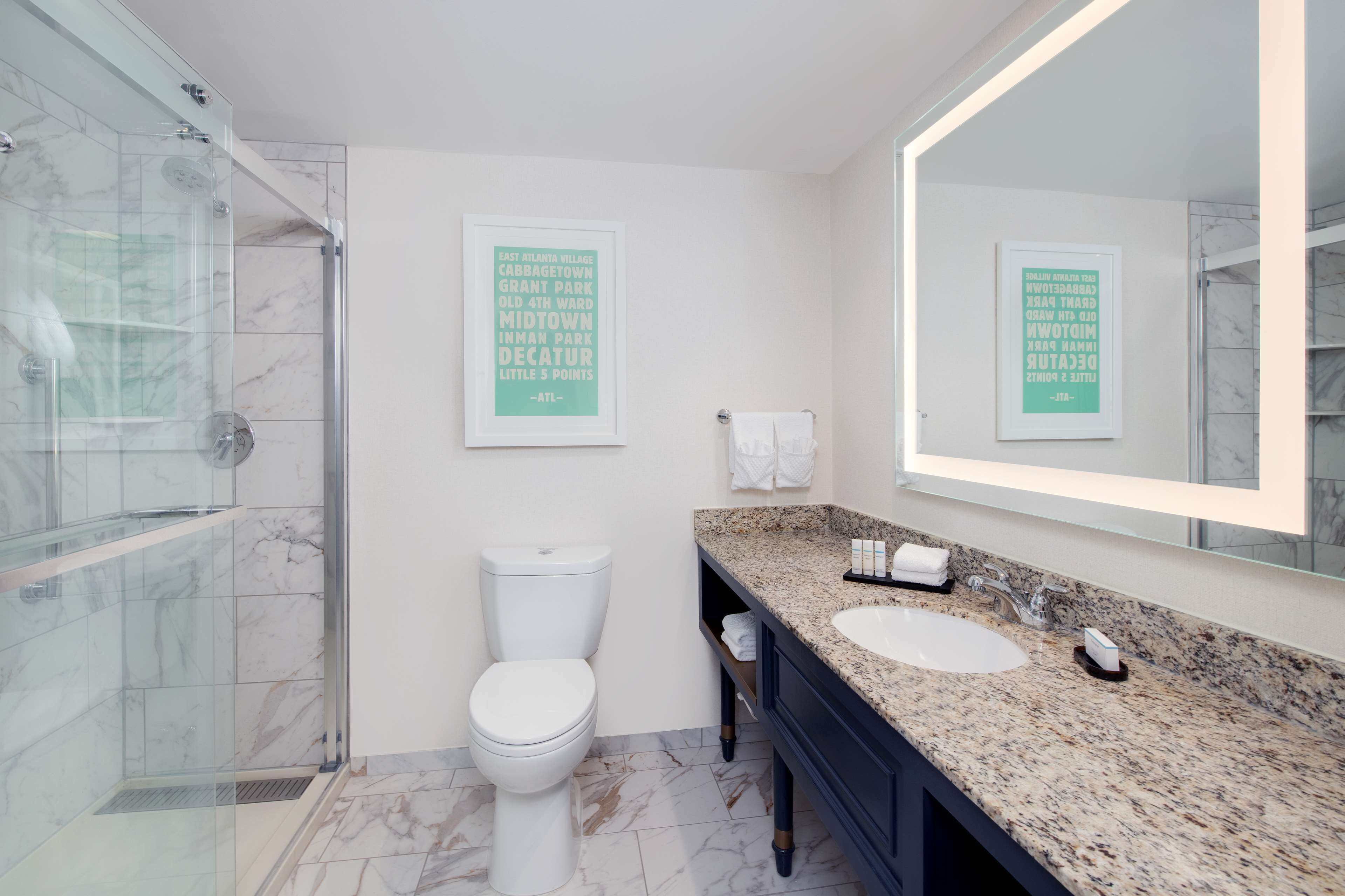 Une salle de bain moderne avec une douche à parois de verre, des toilettes blanches, un lavabo sur un plan de travail en granit et un grand miroir.