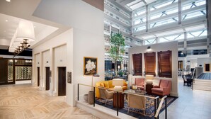 A spacious lobby with a herringbone floor, a central seating area with a sofa and armchairs, a large window with a view of the sky, and a staircase leading to upper floors. - Embassy Suites by Hilton Atlanta Buckhead (Atlanta)