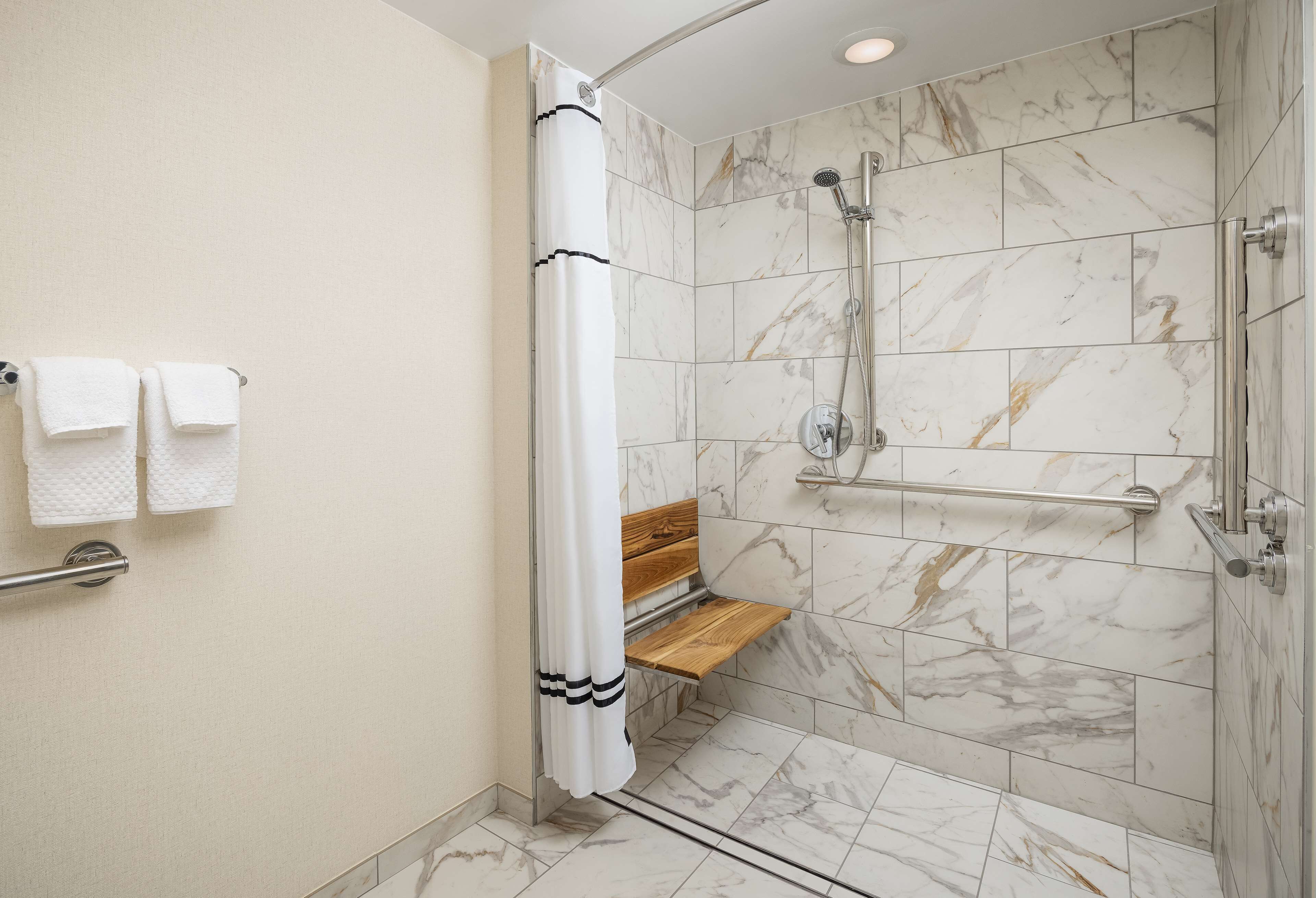 A modern shower with a wooden bench, marble tiles, and a grab bar.