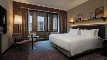 A hotel room with a large bed, a chair, a small table, and a TV.