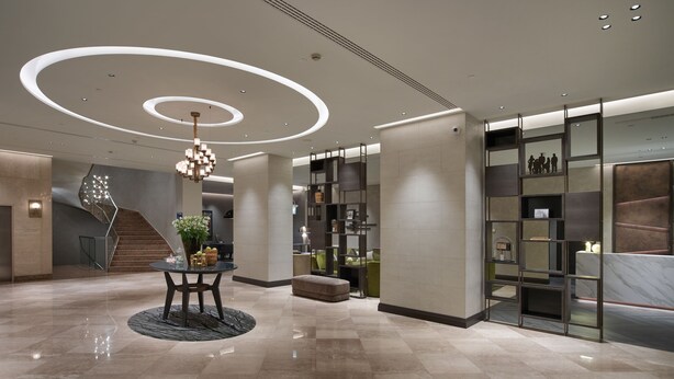 Eine moderne Lobby mit einem runden Kronleuchter, einer Treppe und einer Rezeption.