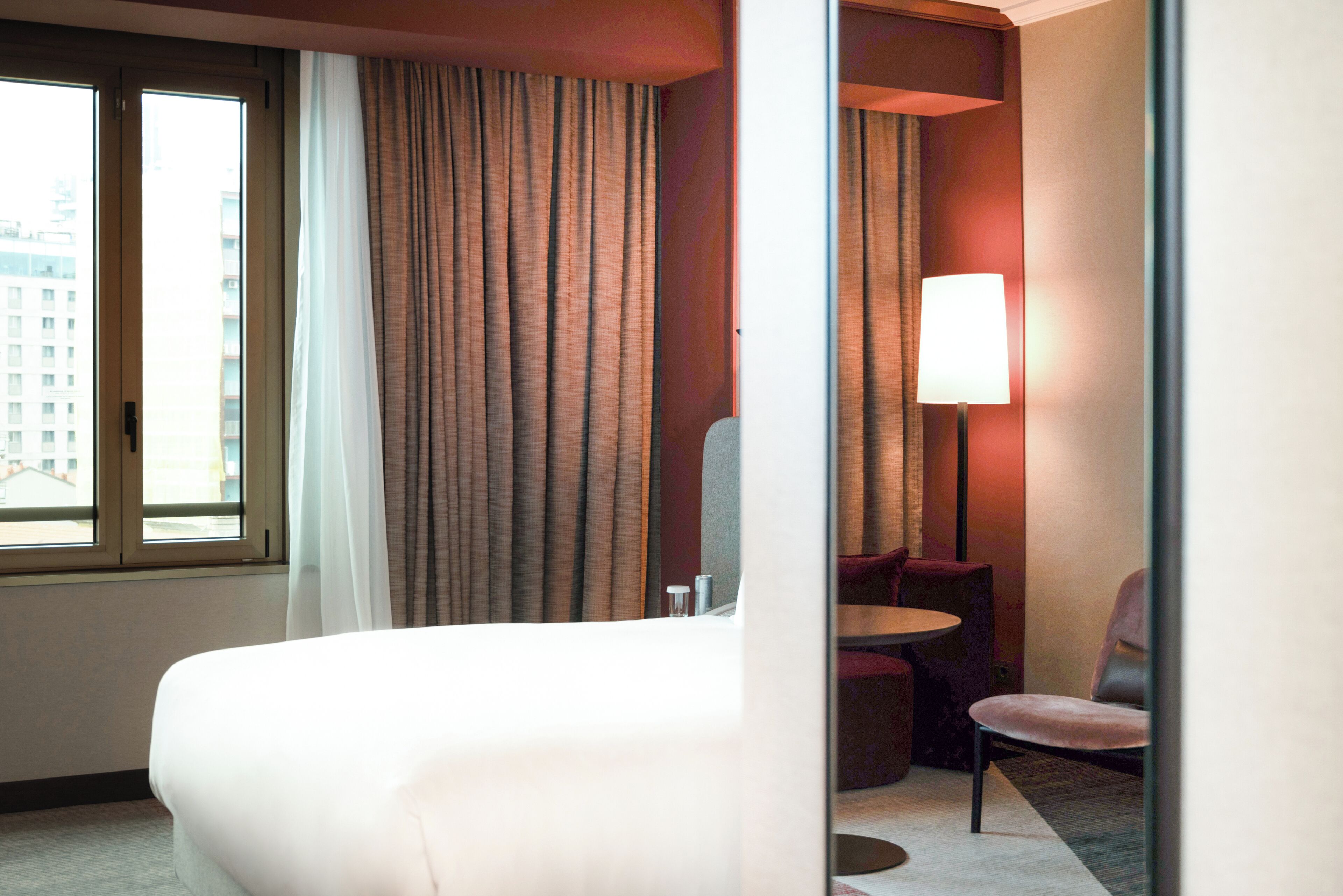 A hotel room with a large bed, a small round table, a chair, and a lamp.