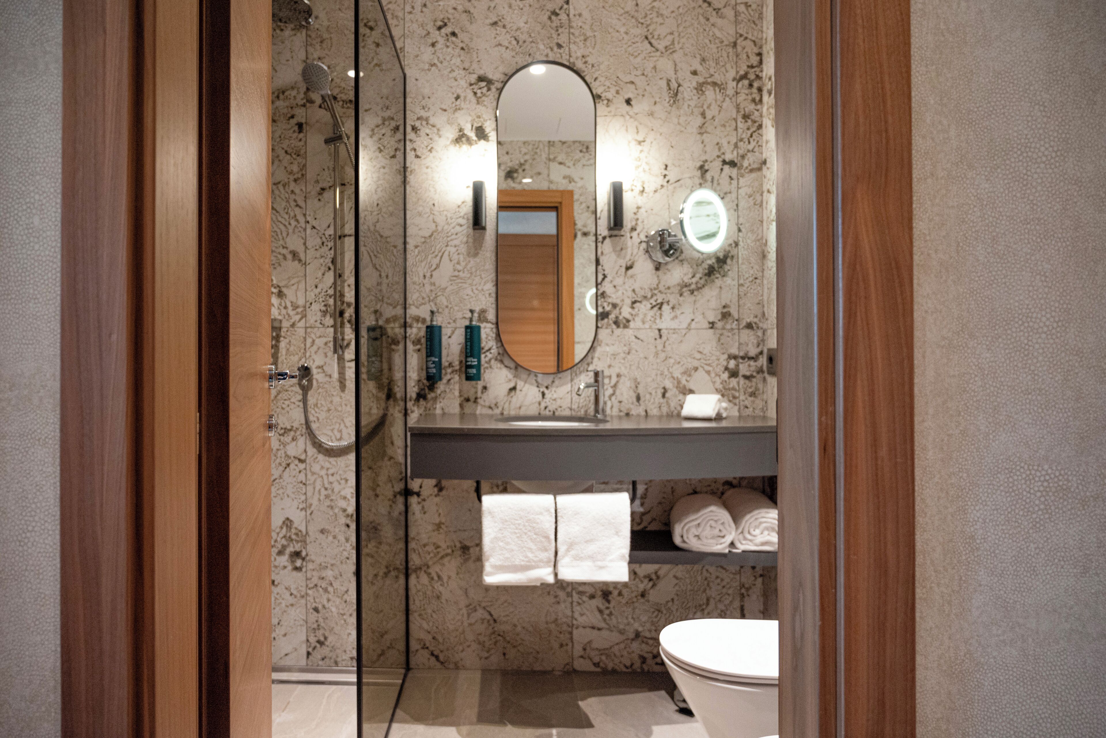 Un baño con cabina de ducha de vidrio, tocador de madera, protector contra salpicaduras de mármol y un inodoro.