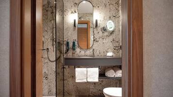 Un baño con cabina de ducha de vidrio, tocador de madera, protector contra salpicaduras de mármol y un inodoro.