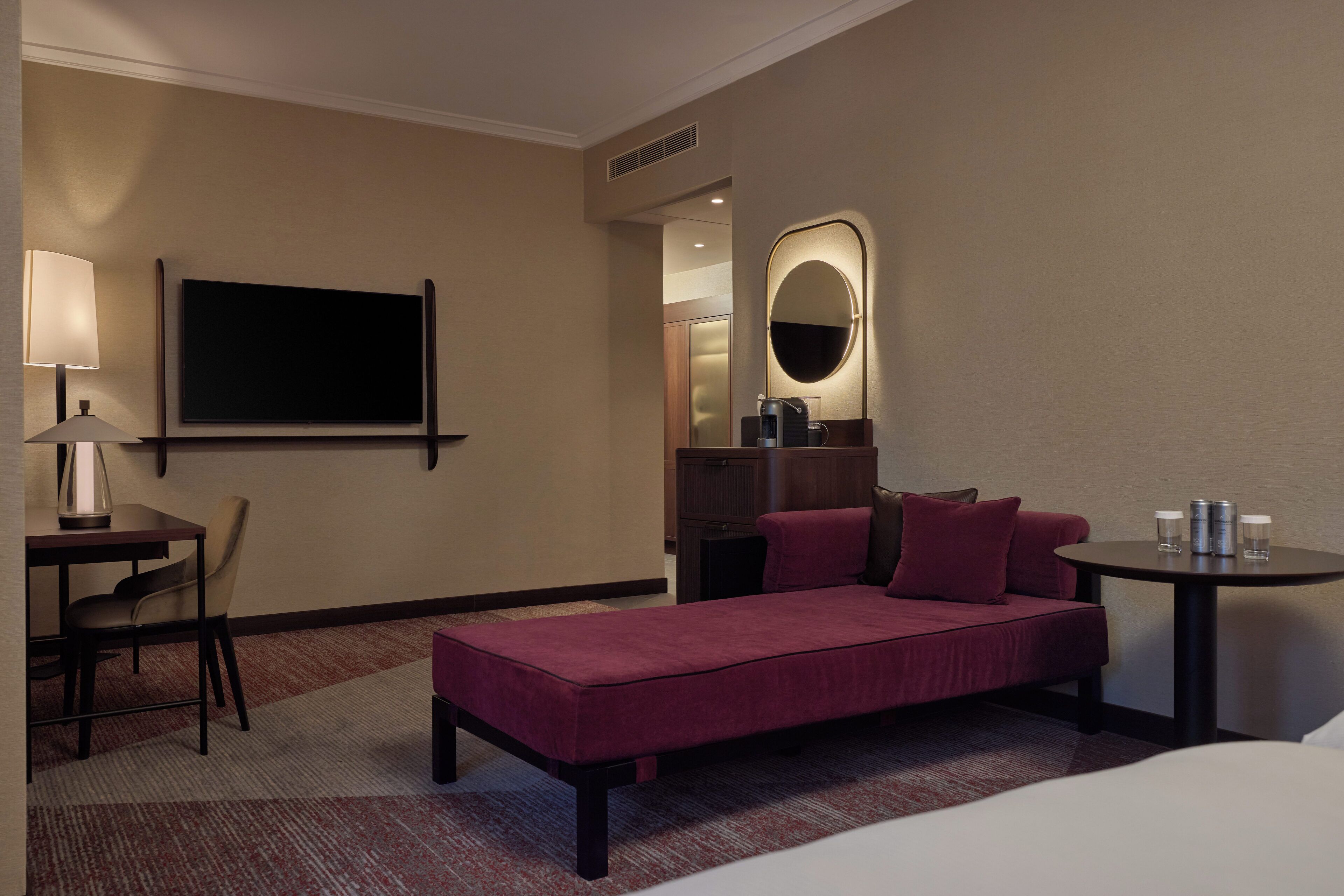 Une chambre d’hôtel avec un lit, un bureau doté d’une lampe, une télévision, une table ronde avec des canettes et un miroir.
