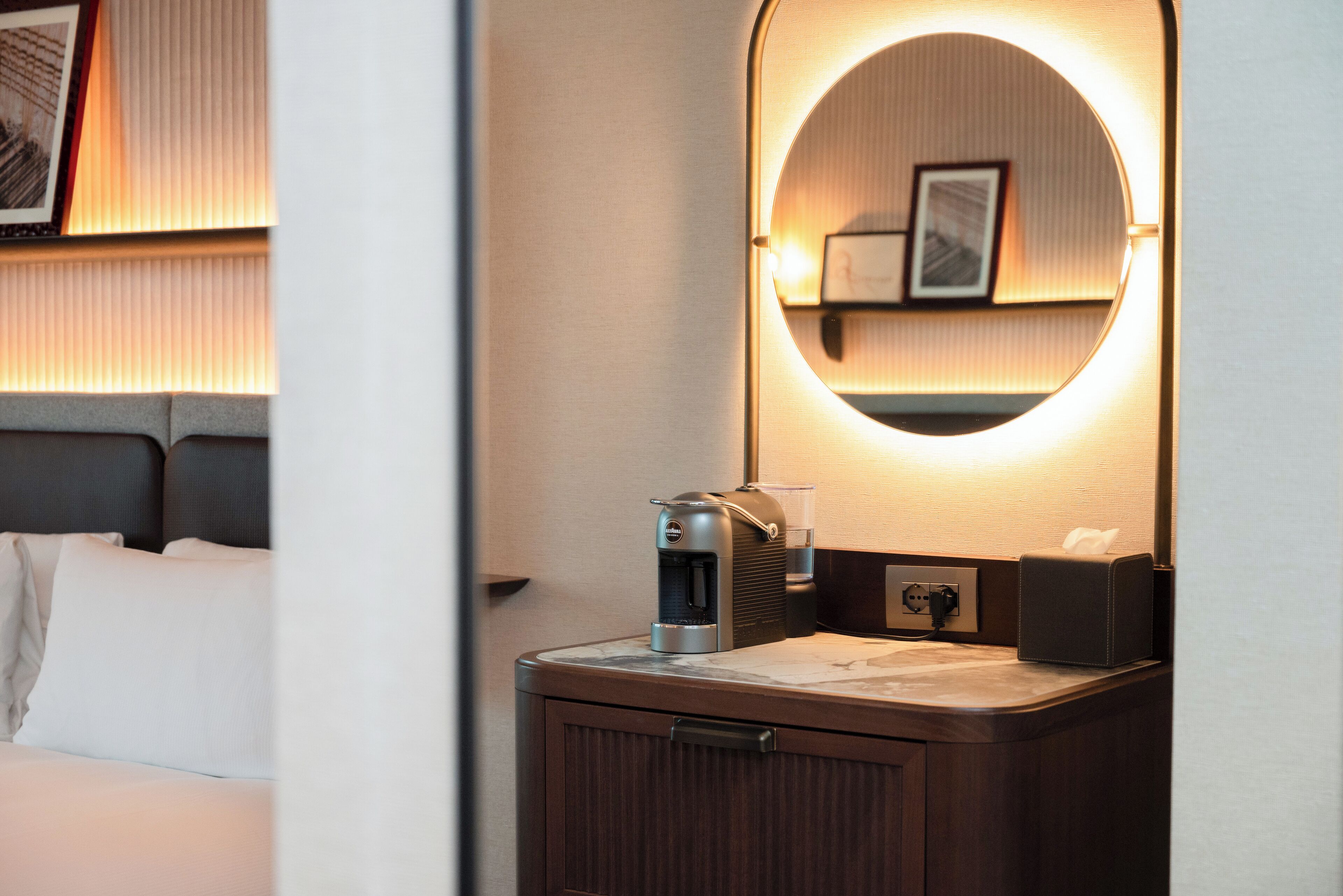 Una habitación de hotel con una cama, una máquina de café, una caja de pañuelos y un espejo con luz.