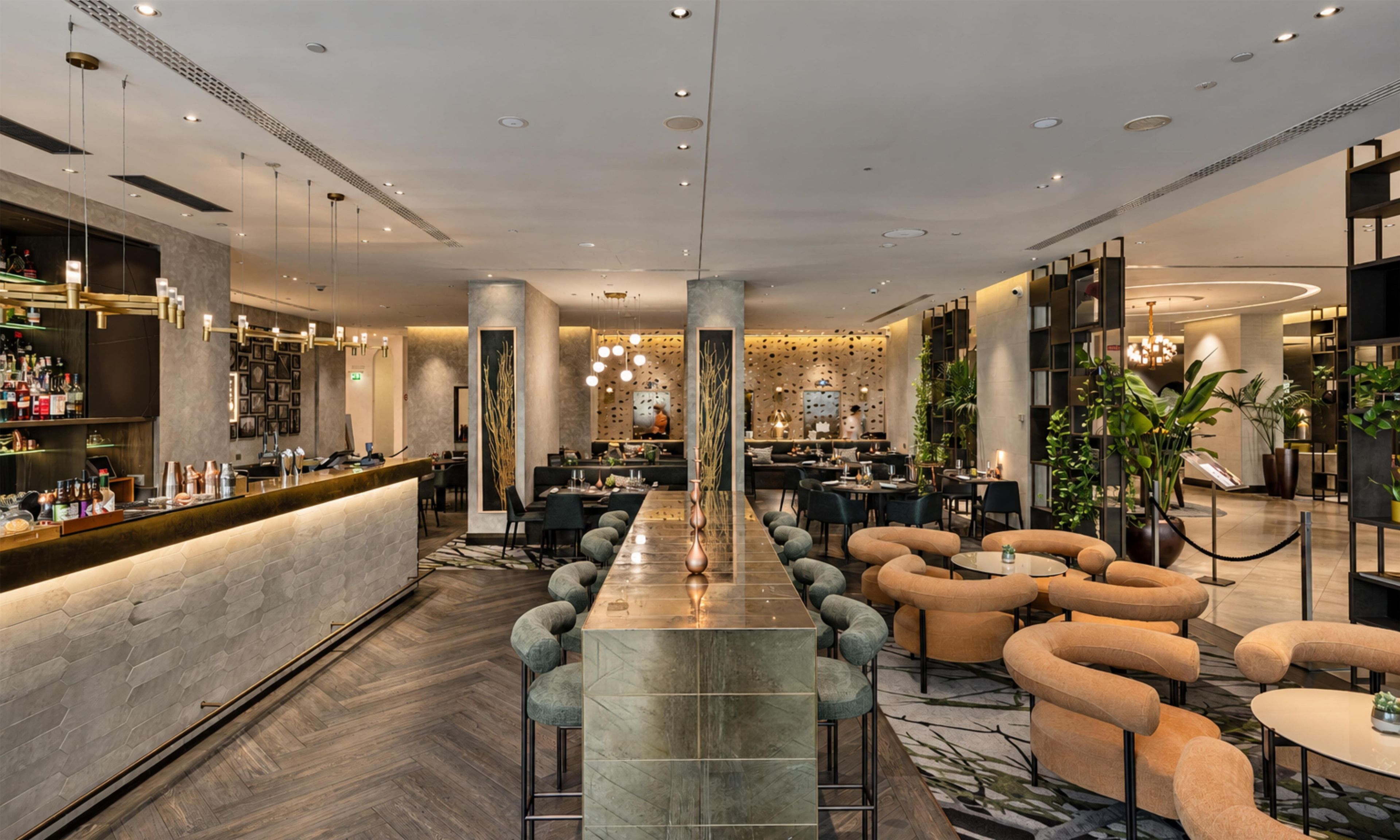 Un espace bar moderne doté d’un long comptoir, de nombreux espaces pour s’asseoir, notamment des canapés et des fauteuils, et d’une colonne centrale décorative.