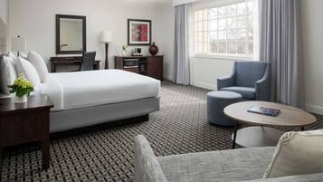 Habitación de hotel con una cama grande, un escritorio con silla, una mesita y una ventana con cortinas.