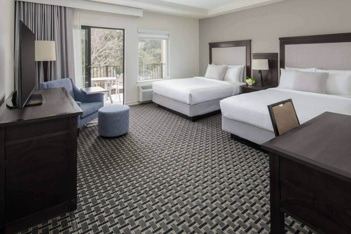 A hotel room with a large bed, a smaller bed, a sofa, a TV, and a desk.